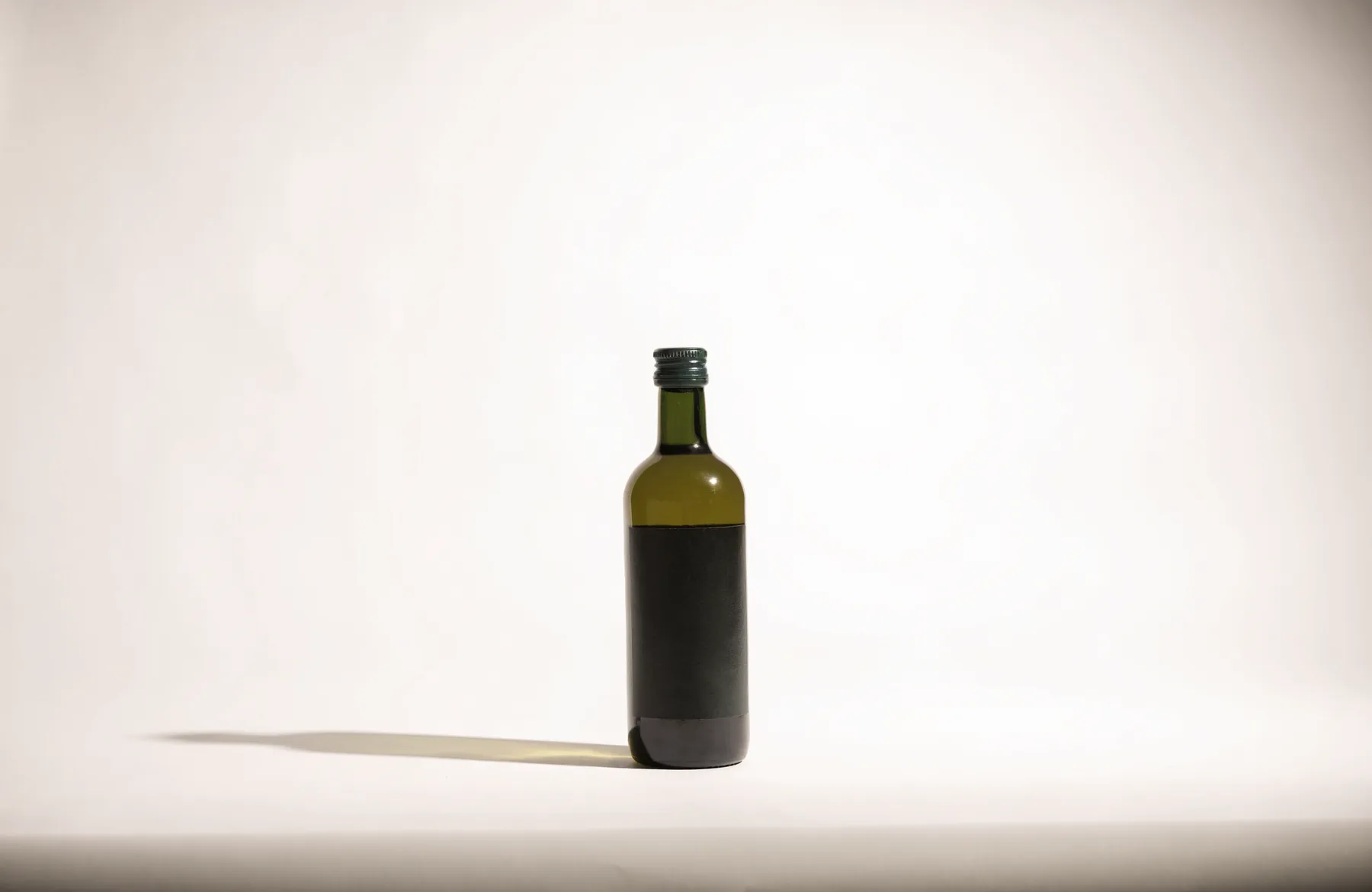 Eine Flasche Olivenöl auf knochenweißem Papiergrund im weichen Studiolicht